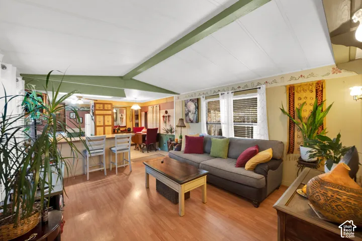 Open floor plan featuring wood-finish flooring, vaulted ceilings with exposed structural beams, and an integrated breakfast bar