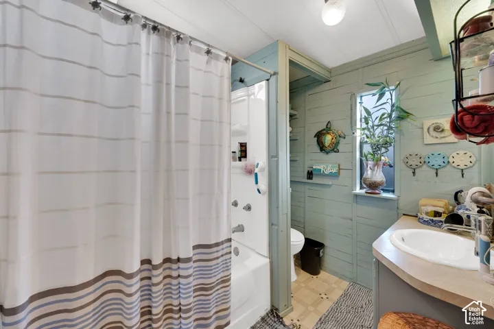 Bathroom featuring painted wood plank walls, a white composite tub surround with integrated shelving, a rounded vanity sink with a laminate countertop, and a vertical window