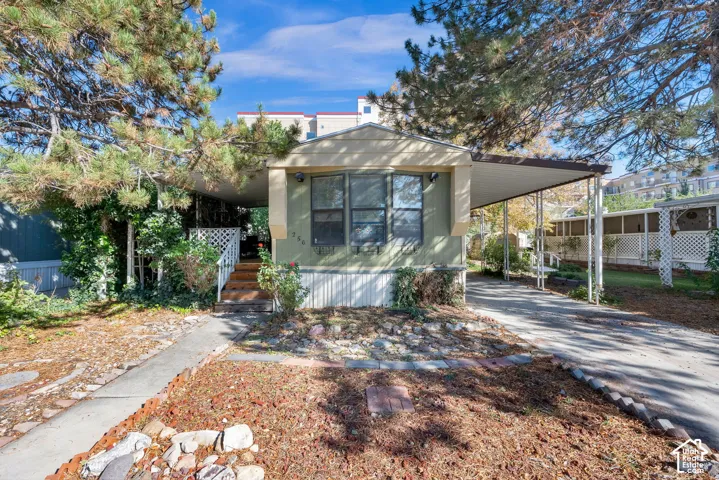 Exterior featuring earth-toned siding, attached covered carport, concrete driveway, and front entryway with wooden stairs