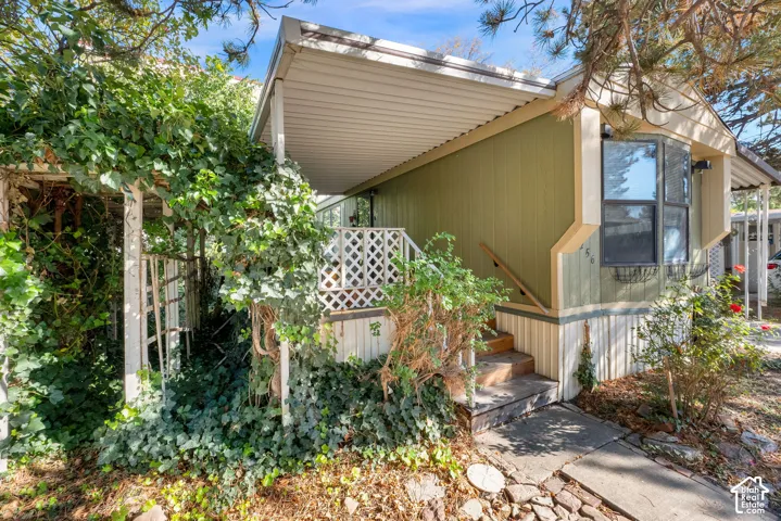 Covered entryway featuring a lattice railing, exterior metal siding, and a wooden staircase