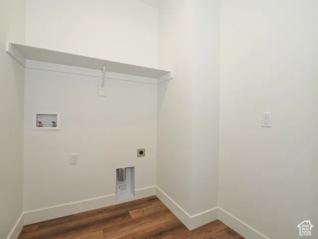 Utility space featuring wood-finish flooring, a built-in overhead shelf, and recessed water and dryer vent hookups