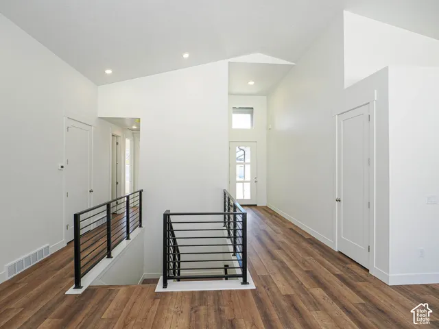 Vaulted ceilings, wood-finish flooring, metal horizontal-bar railings, recessed lighting, and multi-pane entry door