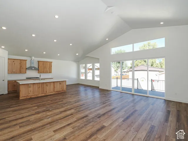 Open-concept living space featuring vaulted ceilings, wood-finish flooring, custom wood cabinetry, a center island with a stone-surface countertop, and glass sliding doors