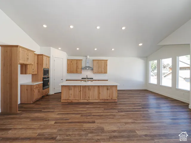 Kitchen featuring natural wood cabinetry, a center island with solid-surface countertops, wood-finish flooring, vaulted ceilings, and recessed lighting