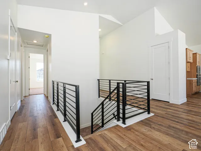 Interior hallway featuring wood-finish flooring, matte black metal horizontal railing, vaulted ceilings, and recessed lighting