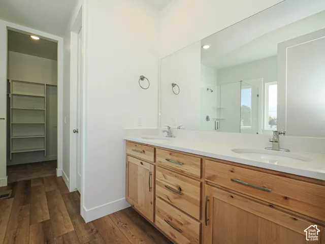 Dual-vanity cabinetry with natural wood finish, stone-surface countertops, integrated undermount sinks, full-width vanity mirror, and wood-finish flooring