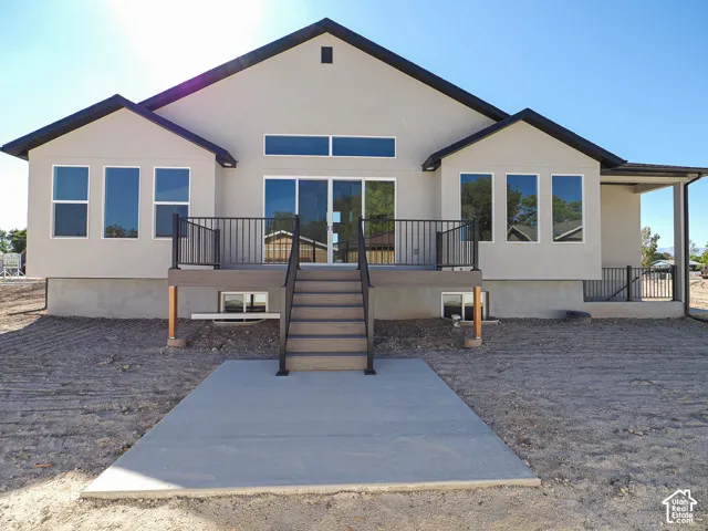 Stucco exterior featuring an elevated deck with metal railing, concrete patio, and transom windows