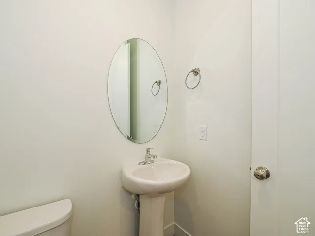Oval wall-mounted mirror, white pedestal sink with chrome faucet, and circular metallic towel ring