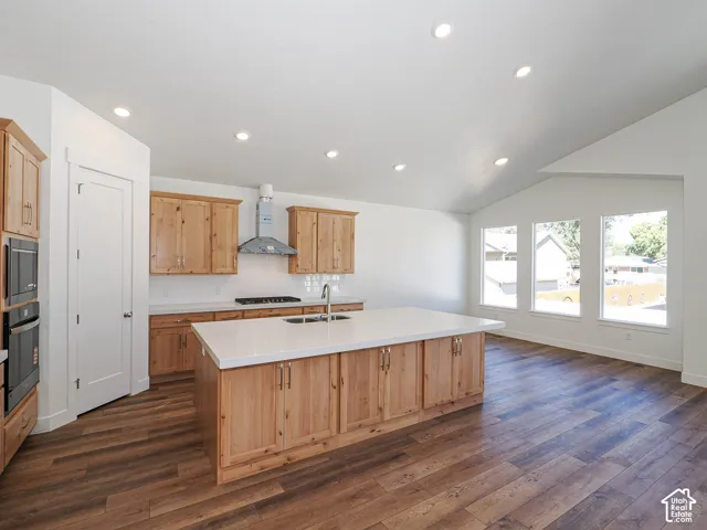 Kitchen featuring wood-finish cabinetry, central island with quartz countertop, wood-finish flooring, recessed lighting, and vaulted ceilings