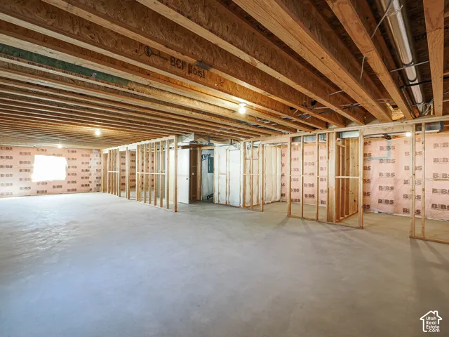 Unfinished open-concept area featuring exposed wooden joists, concrete flooring, insulated wall framing, and vapor barrier detailing