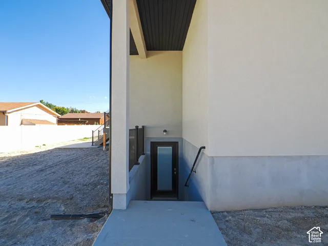 Exterior door with frosted glass panel, concrete stairwell, metal handrail, and dark-toned soffit