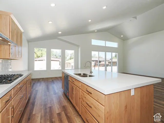 Kitchen featuring natural wood cabinetry, solid-surface countertops, center island with undermount sink, recessed lighting, and wood-finish flooring under a vaulted ceiling