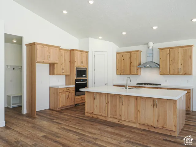 Kitchen featuring wood-finish cabinetry, a large central island with solid-surface countertops, built-in stainless steel oven and microwave, recessed lighting, and wood-finish flooring