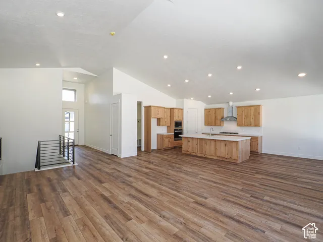Vaulted ceilings, wood-finish flooring, kitchen island with stone countertop, recessed lighting, and metal stair railing