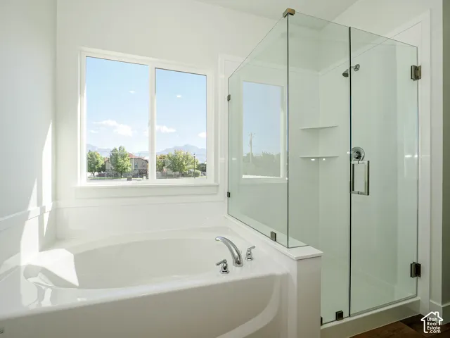 Oval soaking tub with deck-mounted chrome faucet, glass-enclosed shower with built-in shelving, and large window with mountain backdrop
