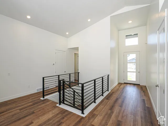 Vaulted ceiling, wood-finish flooring, recessed lighting, matte black metal stair railing, and a multi-pane entry door with a transom window