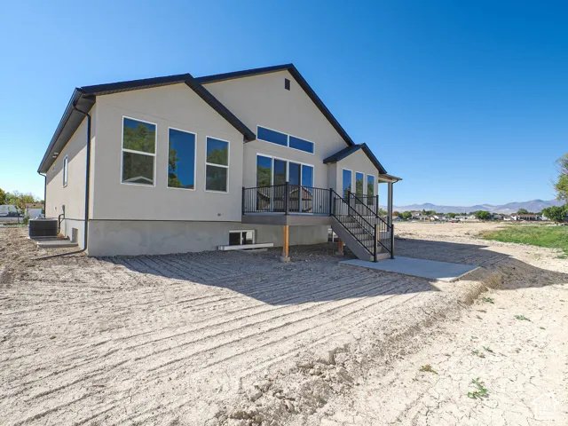 Exterior featuring stucco siding, elevated deck with metal railing, concrete patio, and large glass windows