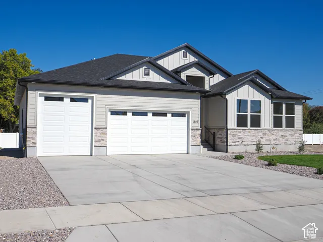Exterior featuring a combination of stone veneer and horizontal siding, multi-gabled roofline with vertical board-and-batten accents, three-car garage, and concrete driveway