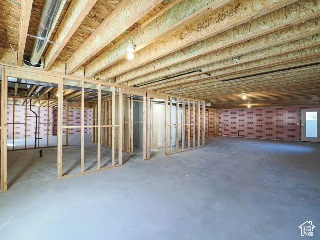 Unfinished interior space featuring exposed wood framing, concrete flooring, pink wall insulation, and overhead structural joists