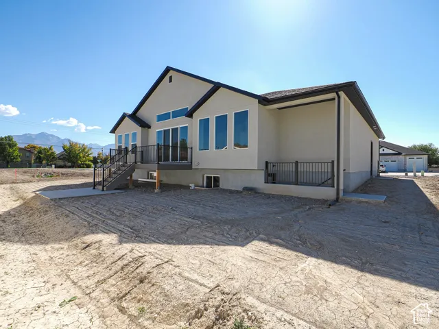 Single-story exterior featuring a light-toned stucco facade, multi-gabled roofline, elevated deck with dark metal railing, large windows with transom accents, and mountain scenery