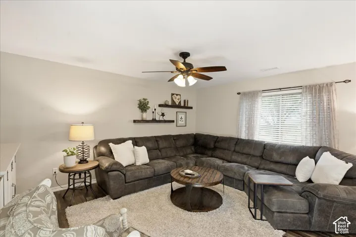 Living area featuring dual wall-mounted floating shelves, a multi-blade ceiling fan with integrated lighting, and horizontal window blinds