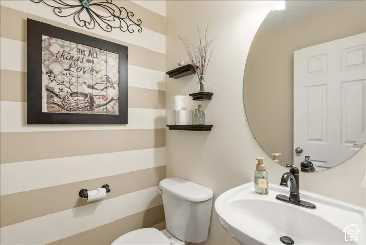 Round wall-mounted mirror, pedestal sink with dark metal faucet, and horizontal striped accent wall