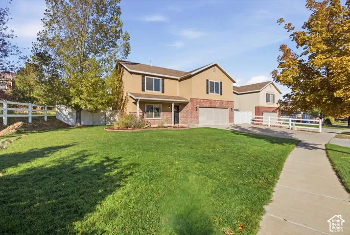 Two-story exterior featuring a brick and stucco facade, an attached two-car garage, and white perimeter fencing