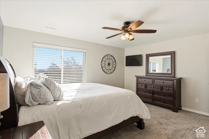 Neutral wall paint, plush carpeting, large window with horizontal blinds, and a multi-blade ceiling fan with integrated lighting