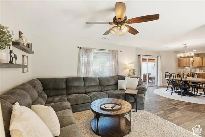 Living area featuring wood-finish tile flooring, ceiling fan with integrated lighting, wall-mounted floating shelving, and sliding glass patio doors