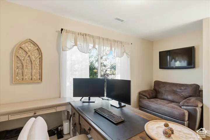 Neutral-toned room featuring a wide window with natural light, wall-mounted television, and built-in desk cabinetry