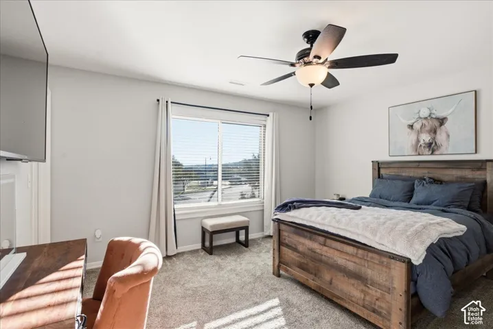 Neutral-toned room featuring a central ceiling fan with integrated lighting, carpeted flooring, and a large sliding window