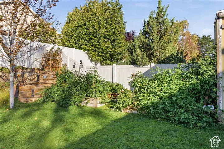 Backyard featuring a tiered stone retaining wall, raised garden beds, and white vinyl privacy fencing