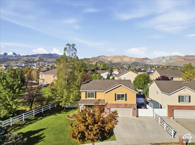 Two-story residence featuring a brick and stucco exterior, attached two-car garage, concrete driveway, and expansive lawn area enclosed by white vinyl fencing