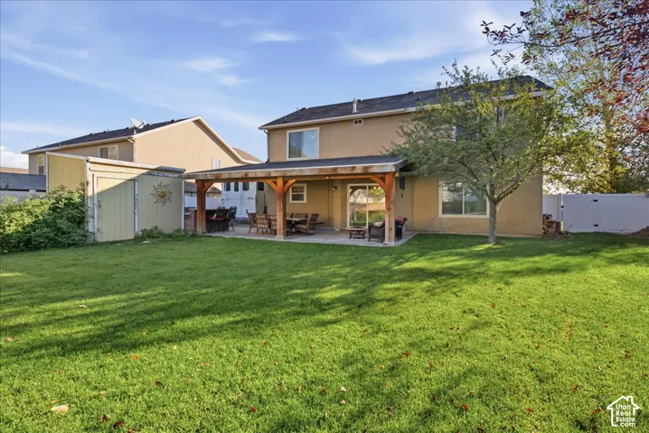 Expansive backyard featuring a manicured lawn, covered patio with timber support beams, and a detached storage structure