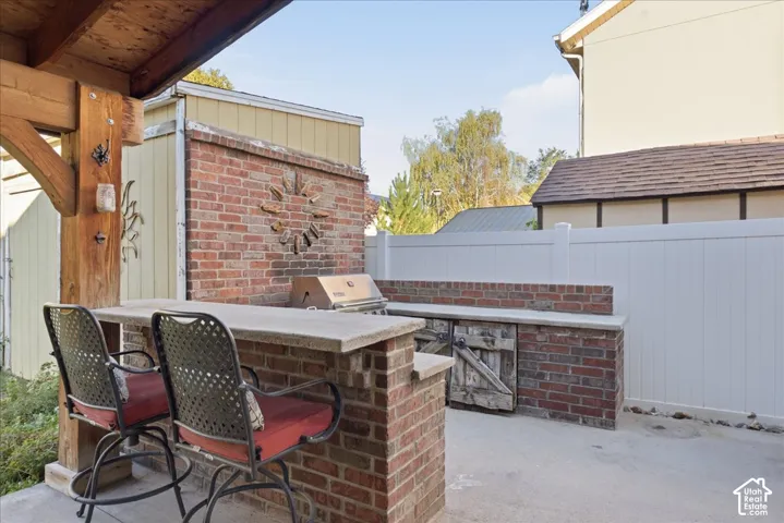 Outdoor kitchen featuring a brick structure, built-in stainless steel grill, stone-finish countertop, wood-post pergola, and concrete patio