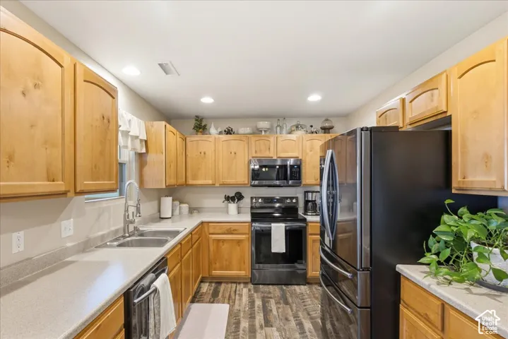 Kitchen featuring light wood-finish cabinetry, solid-surface countertops, dual-basin stainless steel sink with gooseneck faucet, integrated stainless steel microwave, and wood-finish flooring