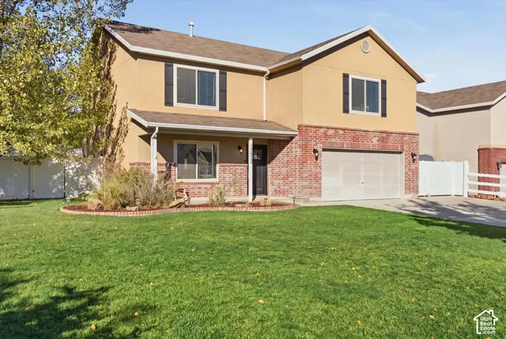 Two-story exterior featuring a brick and stucco facade, an attached two-car garage, and a manicured front lawn with a decorative landscape bed