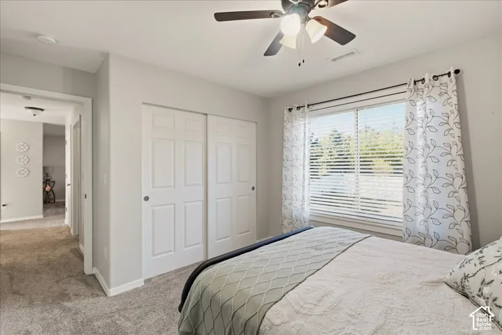 Neutral interior featuring wall-to-wall carpeting, sliding panel closet doors, a multi-light ceiling fan, and a dual-pane window with adjustable blinds