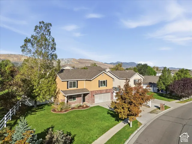 Two-story residence featuring a brick and stucco exterior, an attached two-car garage, mature trees, and a mountain backdrop