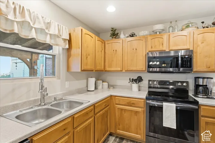 Kitchen featuring natural wood cabinetry, stainless steel appliances, double-basin undermount sink, and stone-composite countertops