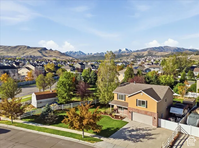 Two-story residence featuring a brick and stucco exterior, attached two-car garage, white vinyl fencing, and mature trees against a mountain backdrop