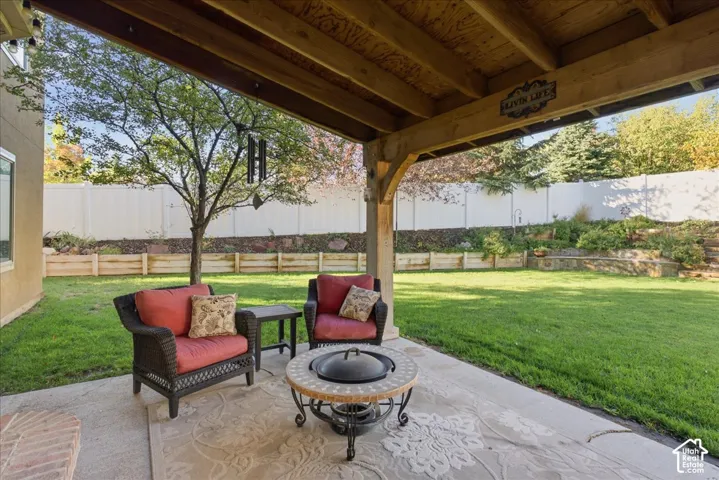Covered patio with exposed timber framing and concrete flooring, featuring a fenced backyard, tiered retaining walls, and mature landscaping