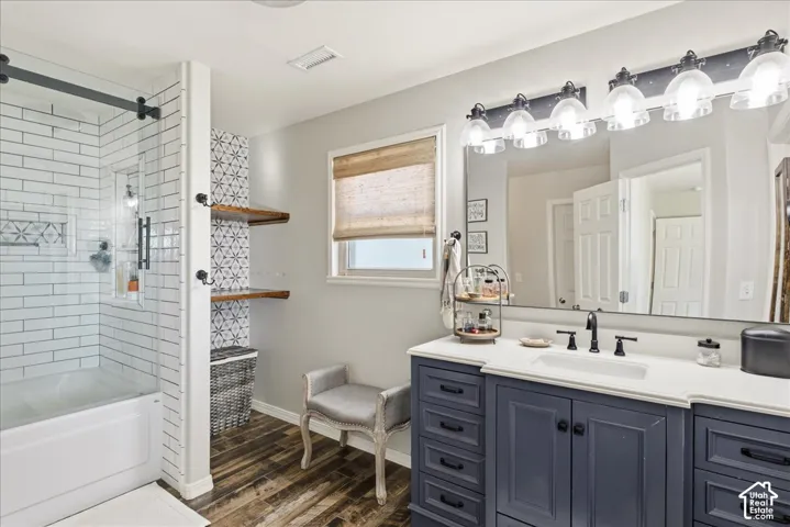 Bathroom featuring a sliding glass shower door, white subway tile surround, custom wood-finish shelving, dark-toned cabinetry with a solid-surface countertop, and a multi-bulb vanity light fixture