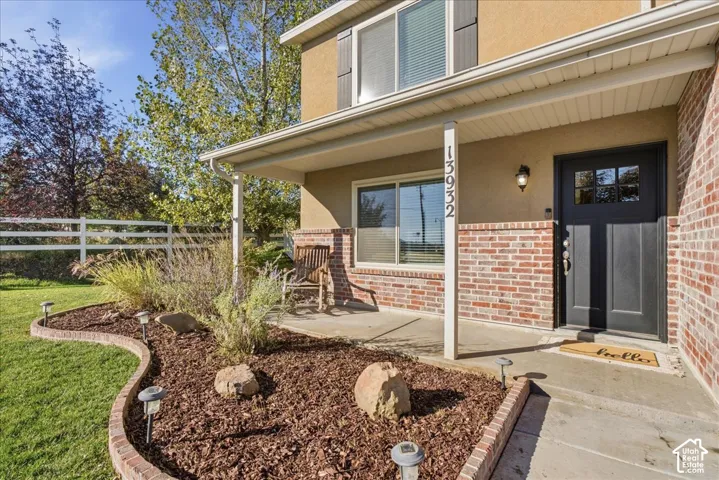 Covered front porch featuring a concrete foundation, brick veneer accents, a dark-toned paneled entry door, and a landscaped bed with masonry edging