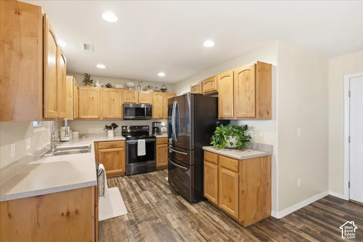 Kitchen featuring wood cabinetry, integrated stainless steel appliances, solid-surface countertops, recessed lighting, and wood-finish flooring