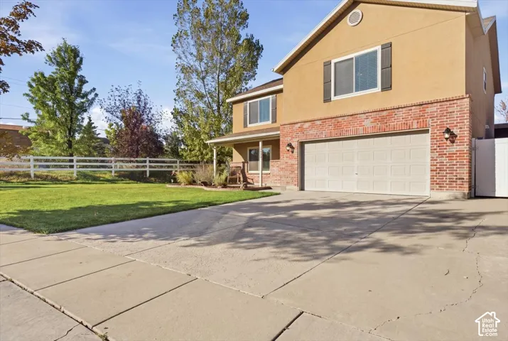 Two-story residence featuring a brick and stucco exterior, attached two-car garage, concrete driveway, and white picket-style perimeter fencing