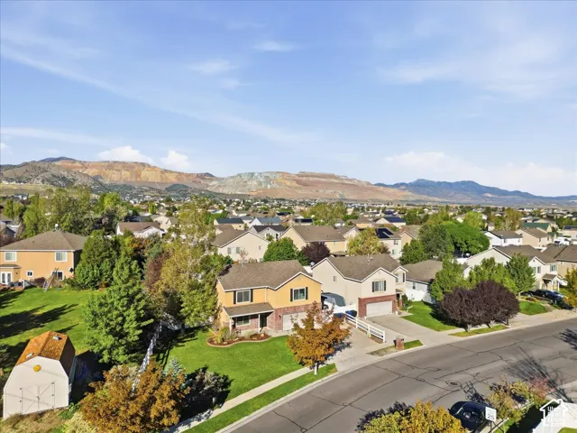 Two-story residential exterior with a brick and stucco facade, attached garage, detached storage shed, manicured lawn, and mountainous horizon
