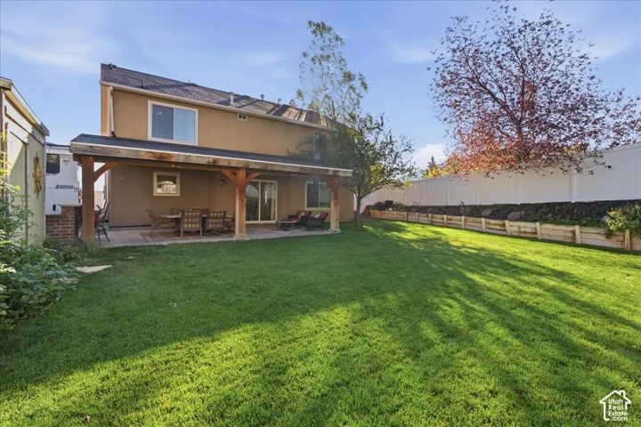 Expansive backyard featuring a manicured lawn, a covered patio with timber support beams, and tiered retaining walls