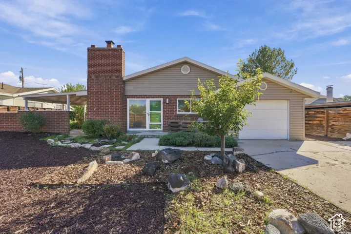Single-story residence featuring a brick chimney, vinyl siding, attached one-car garage, covered side patio, and xeriscaped front yard with decorative stone accents