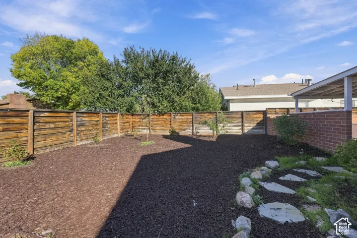 Private backyard featuring a horizontal wood-slat privacy fence, brick exterior wall, mulched landscape beds, and natural stone paver pathway